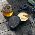 Tub of 'Fire Horse Botanicals' product  with a jar of honey on a wooden surface with lavender flowers.