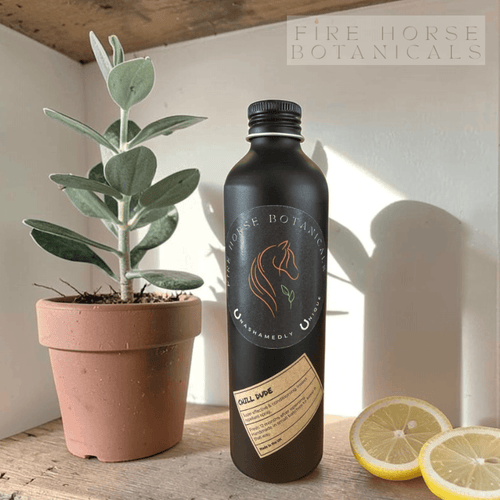 Black bottle with 'Fire Horse Botanicals' label next to a potted plant and lemons on a wooden surface.