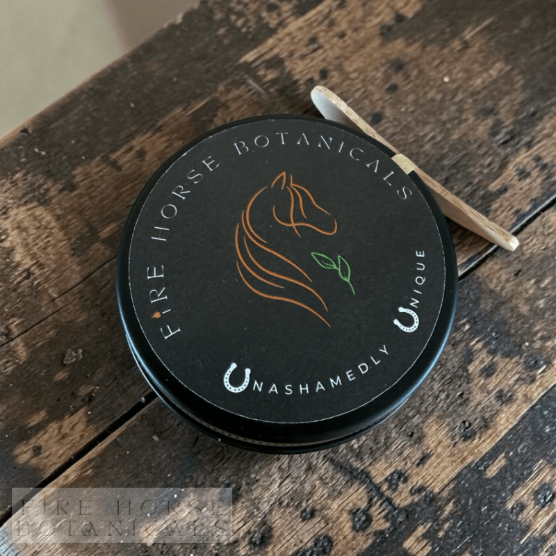 Black tin of 'Fire Horse Botanicals' healing balm on a wooden surface.