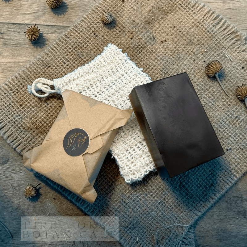 Bar of soap and second bar wrapped in brown paper on textured surface with 'Fire  Horse Botanicals' branding.