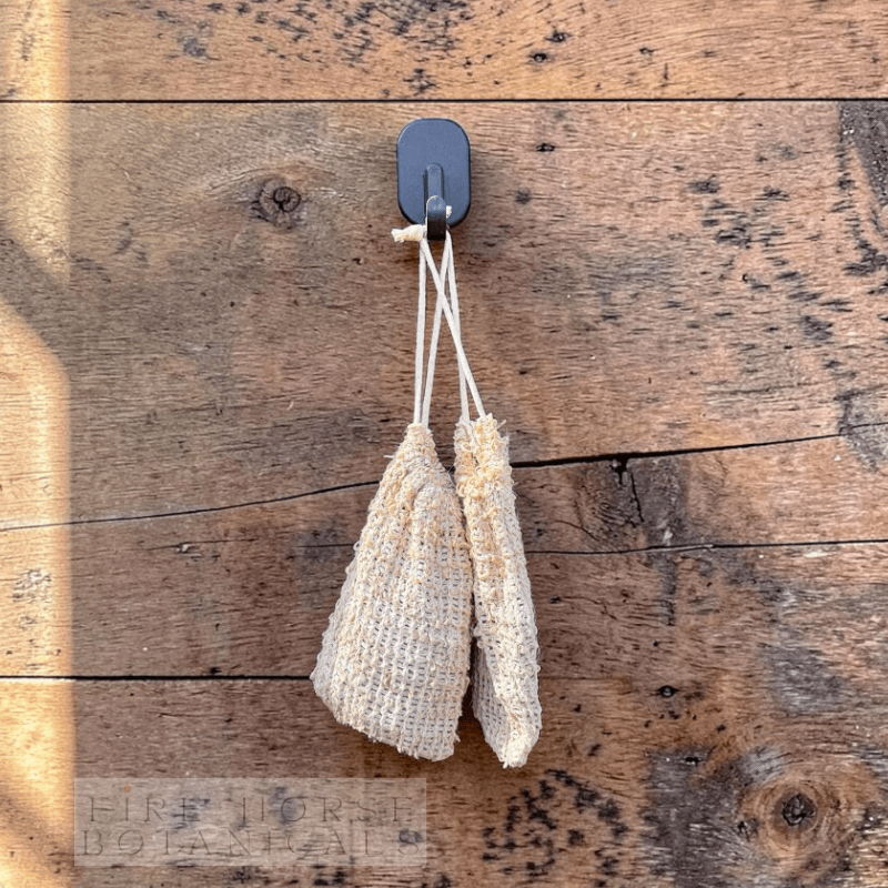 Two sisal soap bags hanging from a hook on a wooden surface with 'Fire Horse Botanicals' branding